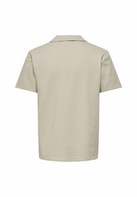 Polo shirt beige a maniche corte con tessuto testurizzato, caratterizzato da un colletto piatto e un orlo dritto. Senza motivi o decorazioni visibili.