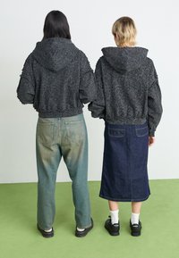 Two individuals wear cropped, textured black hoodies with a distressed look. One pairs it with faded blue jeans, the other with a dark denim skirt.