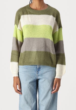 Personne portant un pull en maille côtelée avec des rayures horizontales en vert olive, blanc, vert citron et gris, associé à un jean bleu clair.