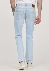 Jeans en denim bleu clair avec une coupe slim, comportant des poches arrière, une patch en cuir brun à la taille et des détails délavés subtils.