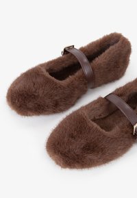 Pantofole di pelliccia marrone con punta arrotondata, texture morbida e una cintura marrone con una fibbia dorata per la chiusura.
