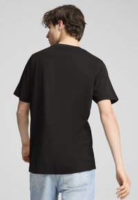 Camiseta de algodón negra con mangas cortas y cuello redondo, que presenta un diseño sencillo y dobladillo recto, combinada con jeans de color azul claro.