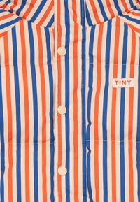 Striped sako s vertikálními pruhy v oranžové, modré a béžové barvě, s zapínáním na knoflíky a štítkem "TINY" vyšitým na boku.