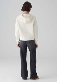 Witte hoodie met een zachte textuur, gecombineerd met donkere flare jeans. De outfit heeft een ontspannen pasvorm en een minimale afwerking.