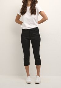 Pantalon noir court au design ajusté, accompagné d'un t-shirt blanc uni et de baskets blanches, créant un look classique et décontracté.