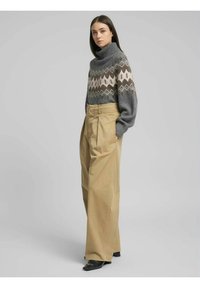 Maglione a collo alto grigio con accenti beige lavorati a motivo, abbinato a pantaloni beige a gamba larga e vita alta. Scarpe basse nere completano il look.