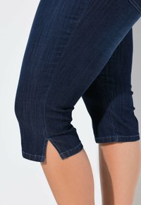 Pantalones capri de mezclilla oscura con un diseño ajustado, que presentan una ligera abertura en el dobladillo y una textura sutil, ideales para el uso casual.