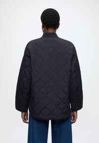 Crna prešivena jakna opuštenog kroja, s rebrastim ovratnikom i spuštenim ramenima, koja ima glatku teksturu i minimalistički dizajn.