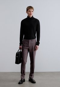 Μαύρο πλεκτό ζιβάγκο, γκρι πλισέ παντελόνι, μαύρη δερμάτινη τσάντα, γυαλισμένα παπούτσια· συνολικά εφαρμοστή γραμμή με καθαρές γραμμές και ελάχιστες λεπτομέρειες.