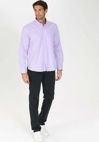 Chemise boutonnée lilas à manches longues, assortie à un pantalon noir slim et des baskets blanches. Design simple avec un col classique.