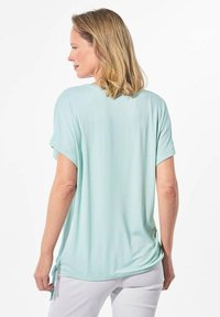 Mintgroene top met korte mouwen, gemaakt van gladde stof, met een relaxte pasvorm, een afgeronde onderkant en zijstrikken voor aanpasbare lengte.