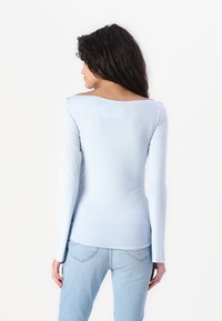 Lyseblå langermet topp laget av mykt stoff, med vid halslinning og samlet sider, kombinert med lyseblå denimjeans.