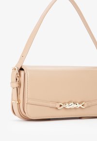 Bolso de mano de imitación cuero beige con una correa larga, forma rectangular y detalle de cadena en tono dorado en la parte delantera. Textura suave y diseño minimalista.