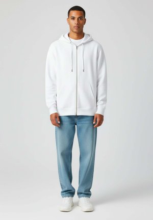 Haut à fermeture éclair blanc avec cordons réglables, poches avant, associé à un jean en denim bleu clair et des baskets blanches. Design simple, texture lisse.