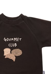 Brown sweatshirt with a crew neck, featuring cartoon drawings of bread and a croissant. Text reads "GOURMET CLUB" in playful white font.