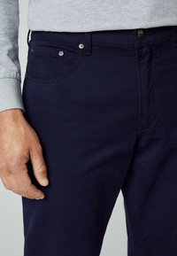 Navyblaue Baumwollhose mit Fronttaschen, Knopfverschluss und Akzentnähten. Der Stoff wirkt glatt und strapazierfähig.