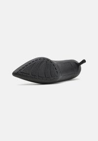 Svart spisssko med teksturert såle, elastisk overdel og bakre trekkstrop, designet for en snug passform og stabilitet.