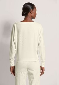 Lichtcrème long-sleeve top met diagonale ribbelstructuur, iets oversized pasvorm en een brede bootnek. Gedetailleerde stiksels zichtbaar.