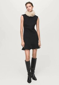 Black sleeveless dress with a flared hem, featuring a soft beige fur collar; worn with knee-high black leather boots.