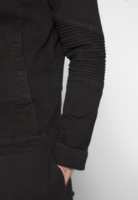 Haut noir à manches longues avec un corps ajusté et une texture côtelée sur les manches. Présente un design épuré et des détails de couture visibles.