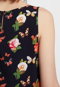 Top sin mangas en tela azul marino, con rosas y mariposas coloridas, y un detalle de botón en la parte trasera del escote.