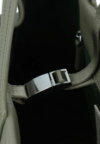 Interno di una borsa in pelle grigia con una chiusura in metallo argentato e un accento verde. Comprende manici in tessuto con una finitura testurizzata. Sfondo scuro.