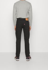 Black jeans with a straight fit and leather patch on the waistband. Paired with a gray long-sleeve shirt and running shoes.