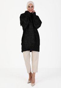 Black textured long sweater with a high neck, paired with beige cropped trousers and nude high heels, set against a white background.