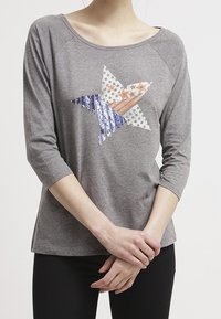 Graues Langarmshirt mit weitem Halsausschnitt, das mit einem mehrfarbigen Sternmuster aus blauen, orangen und weißen Pailletten verziert ist.