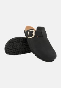 Zoccoli in suede nero con fibbia dorata, plantare in sughero e suola in gomma testurizzata per una buona aderenza. Design minimalista con punta arrotondata.