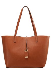 Sac fourre-tout en cuir marron avec deux poignées et une petite étiquette en cuir et ton doré suspendue au centre à l'avant.