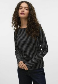 Zwarte langharige shirt met dunne witte strepen, ronde halslijn en aansluitende mouwen, gecombineerd met donkere spijkerbroeken. Zachte stoftextuur is zichtbaar.