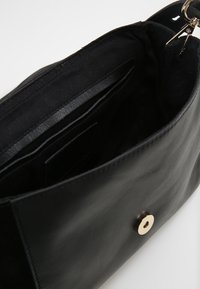 Borsa a tracolla in pelle nera con superficie liscia, dotata di una chiusura a scatto circolare dorata e tasche interne per l'organizzazione.