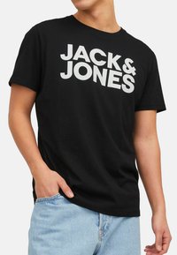 Black t-shirt made of cotton with short sleeves, featuring bold white "JACK & JONES" text across the front. Classic fit.