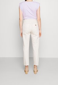 Woman wearing high-waisted off-white jeans with raw hems, a sleeveless lavender top, and nude block-heeled sandals, standing against a light background.