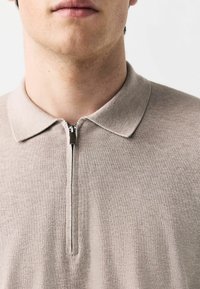 Beige kortærmet polo med lynlås i kraven, ribbet tekstur og klassisk krave, der viser et rent og minimalistisk design.