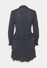 Mörkblå klänning med prickigt mönster, långa ärmar, krage, smockad midja och lager av volang i nederkant. Tyget verkar lätt och texturerat.