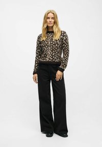 Knitted brown and cream patterned sweater with long sleeves and black wide-leg pants, complemented by black footwear.