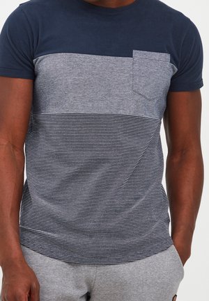 Camicia a maniche corte in misto cotone blu navy e grigio. Presenta una parte superiore blu navy tinta unita e una parte inferiore a righe grigie con una piccola tasca sul petto.