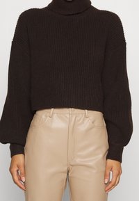 Pull à col roulé côtelé marron avec manches larges, design court, associé à un pantalon beige en similicuir taille haute.