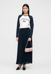 Saia longa plissada azul-marinho combinada com uma t-shirt gráfica branca com mangas raglan azul-marinho. Os acessórios incluem uma pequena mala rosa e saltos pretos.