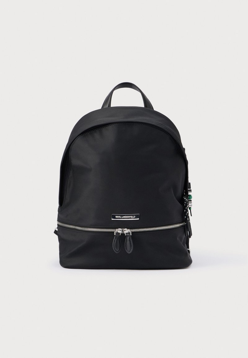 Juodas nailoninis kuprinė su apvaliu viršumi, priekyje užsegama kišenė su užtrauktuku ir dviem užtrauktuko uždarymais. Yra viršutinė rankena ir minimalistinis dizainas.