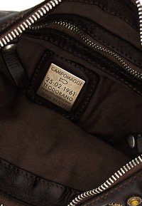 Interno di una borsa in pelle marrone con rivestimento in tessuto, cerniera argentata e etichetta del prodotto con dettagli "Campomaggi" e "Fatto a mano in Italia".