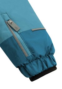 Blauer Stoffärmel mit einem strukturierten Muster, versehen mit einer Reißverschlusstasche in einem kontrastierenden Farbton und einem schwarzen elastischen Bündchen am unteren Ende.