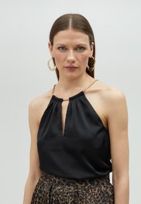 Black satin halter top with keyhole opening, accentuated by a metallic gold neckline detail. Paired with a patterned leopard-print skirt.