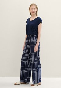 Navy blouse with short sleeves paired with wide-leg, patterned trousers featuring white geometric lines. Smooth fabric texture, casual fit.