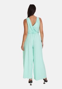 Mintgrøn jumpsuit med plisseret tekstur, nøglehul-ryg og brede ben. Har en tætsiddende talje og ærmeløs design.
