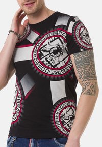 Schwarzes Baumwoll-T-Shirt mit kräftigen grauen und roten geometrischen Mustern, kreisförmigen Designs und kontrastierenden Akzenten im gesamten Stoff.