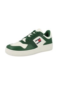 Zapatilla verde y blanca con parte superior de cuero suave, puntera texturizada, diseño con cordones y un parche con el logo que presenta franjas rojas, blancas y azules.