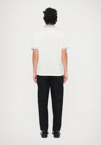 Hvit polotrøye med blå krage, kombinert med svarte bukser og blanke sko. Designet er enkelt og tettsittende, med korte ermer.